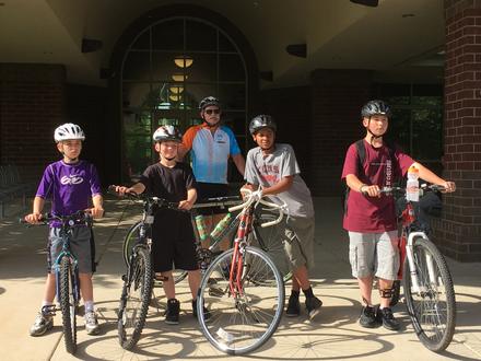 Students in helmets line up with their bikes in front of the school