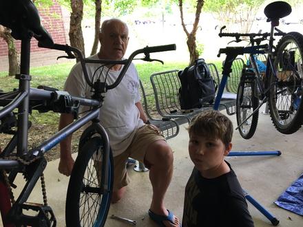 A volunteer kneels to work on a bike while a student looks on